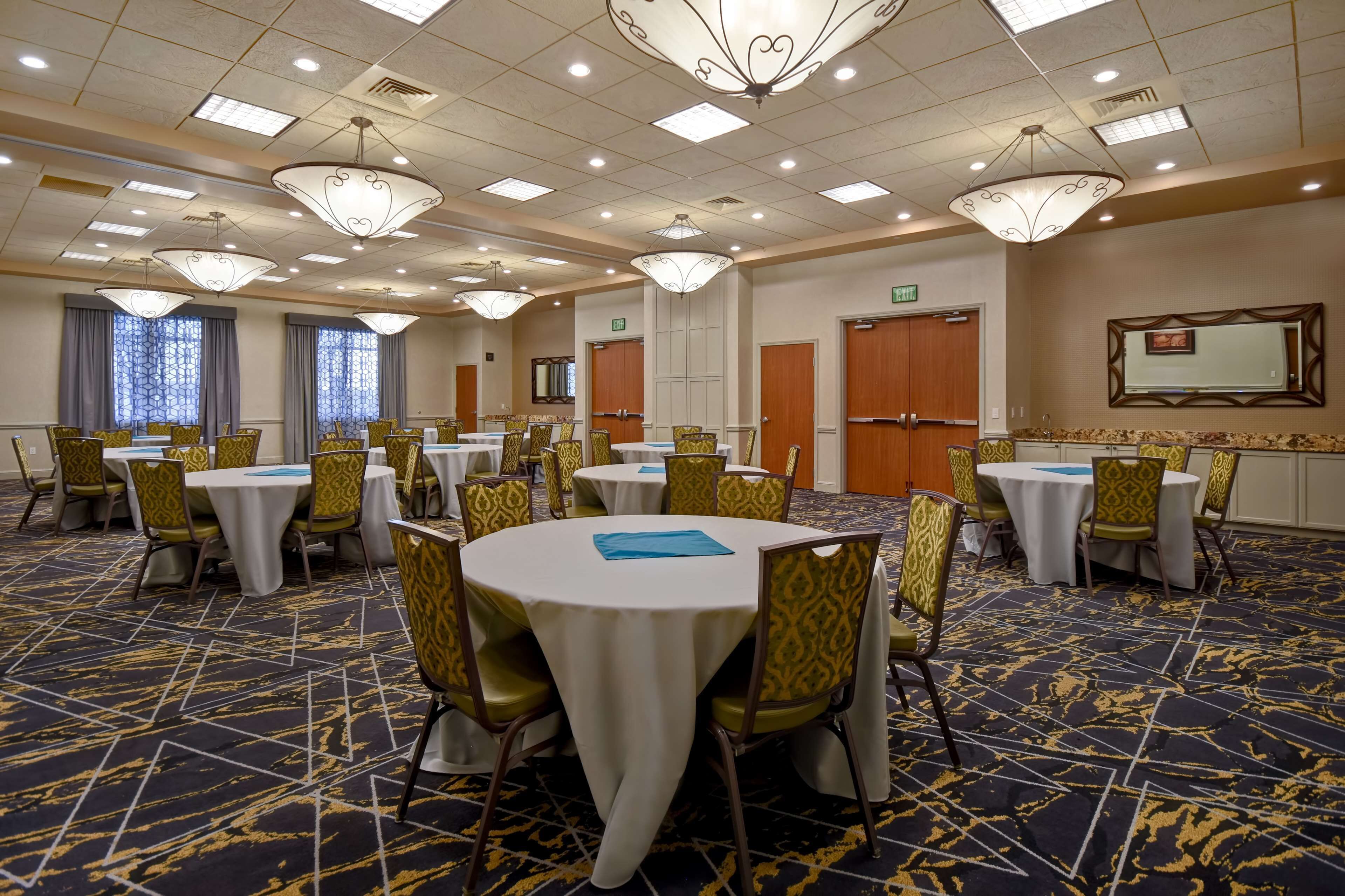 A conference room with round tables and yellow chairs, equipped with white tablecloths and blue placemats.