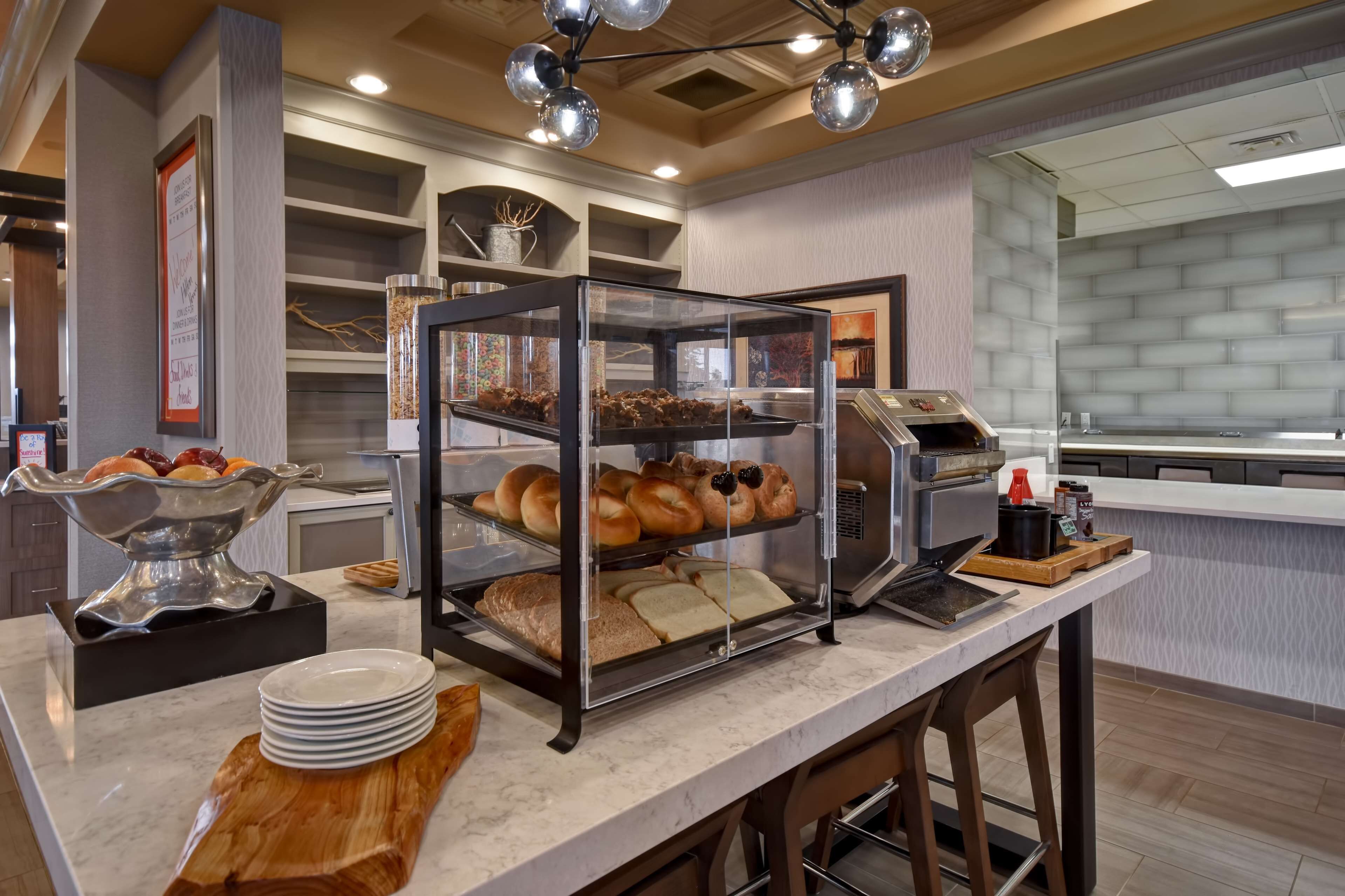A buffet area with a variety of baked goods and pastries displayed in a glass case, a coffee machine, and a condiment station.
