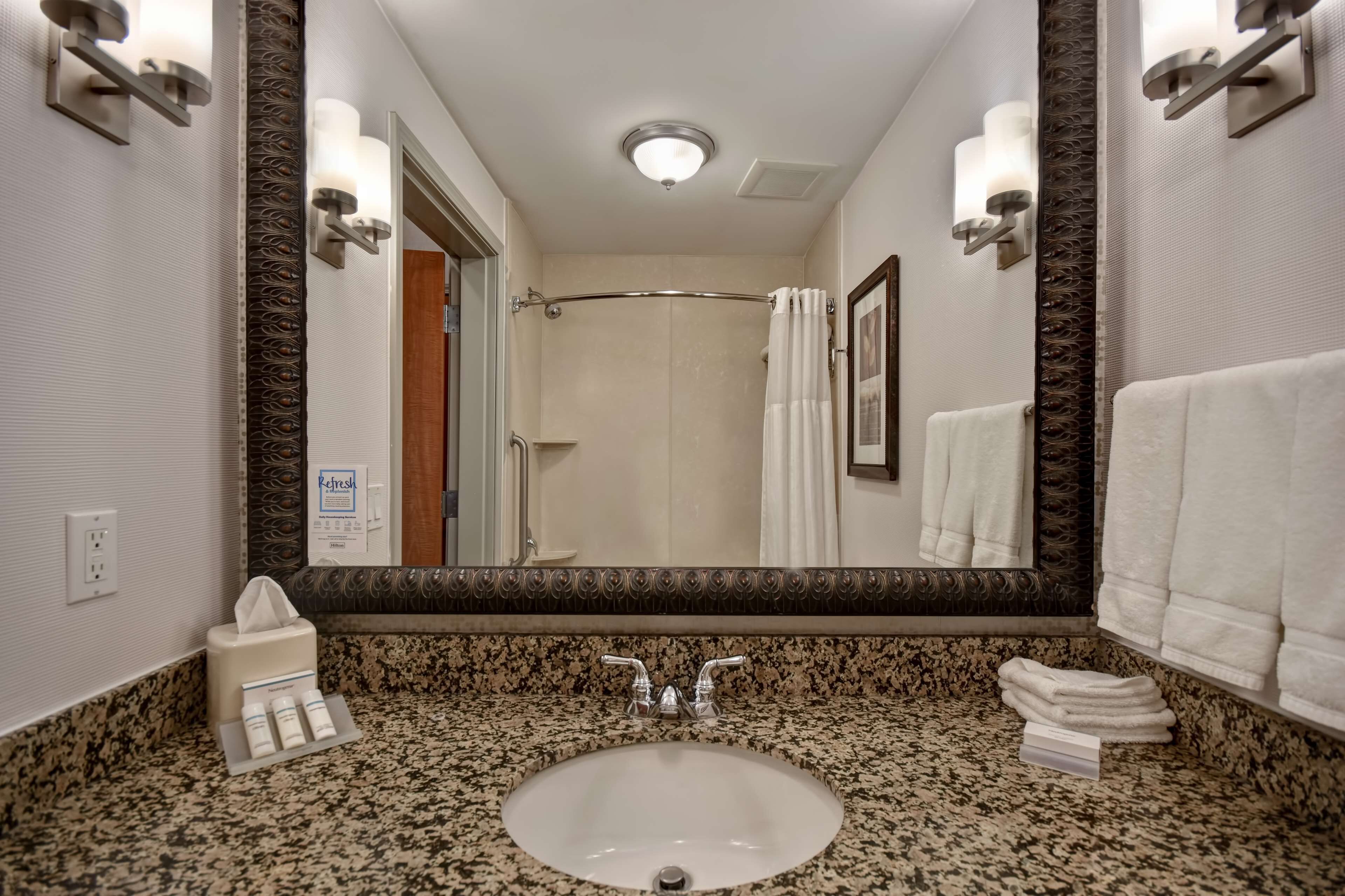 Un baño con encimera de granito, un lavabo, un espejo y una cortina de ducha.
