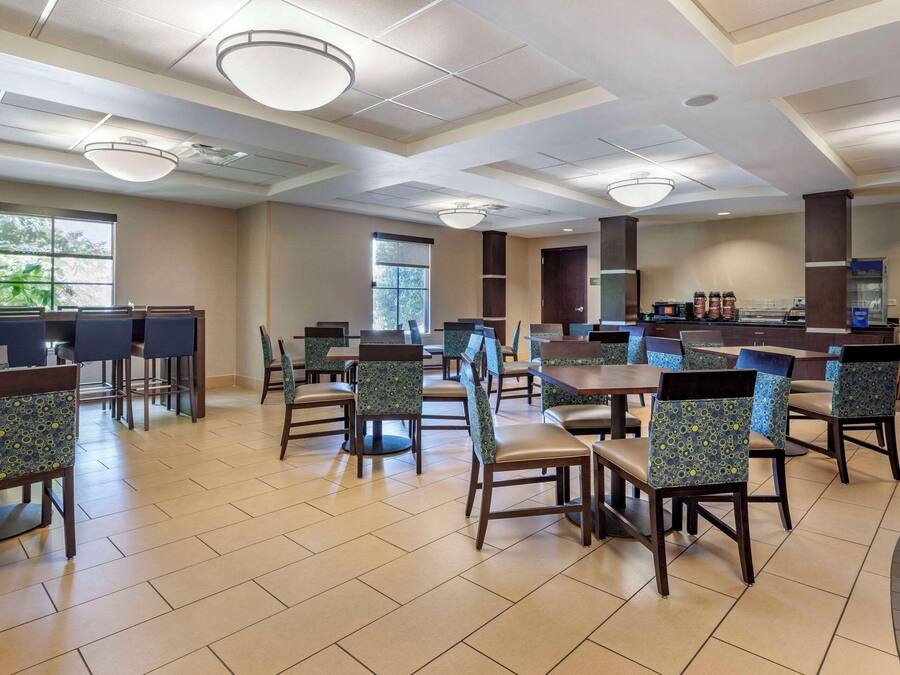 A spacious dining area with multiple tables and chairs, large windows, and a counter with a coffee station.