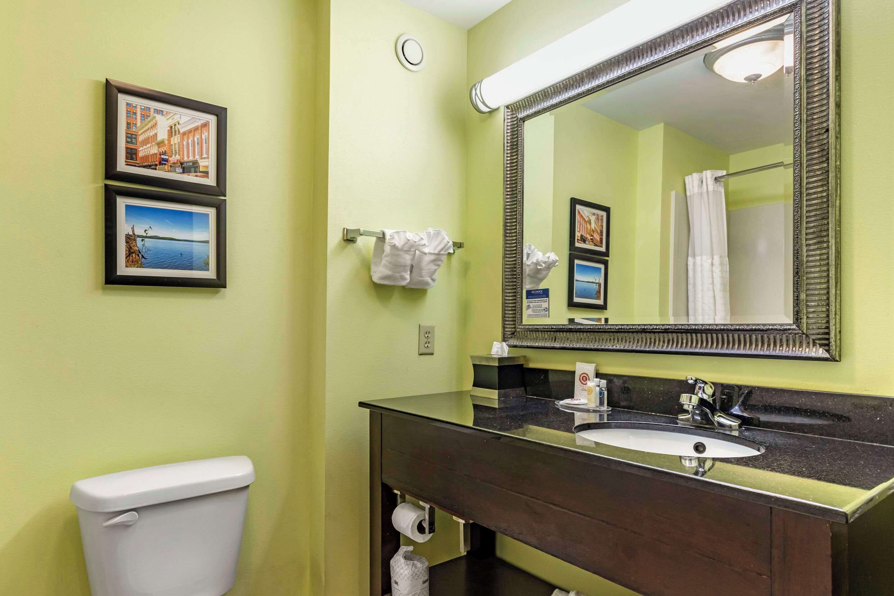 A bathroom with a toilet, sink, and mirror. There are framed pictures on the wall.
