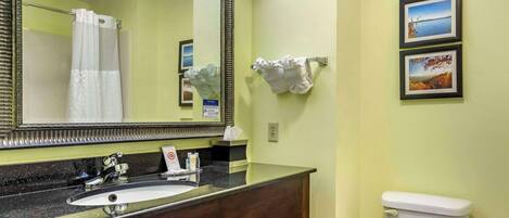 A bathroom with a sink, mirror, toilet, and two framed pictures on the wall.