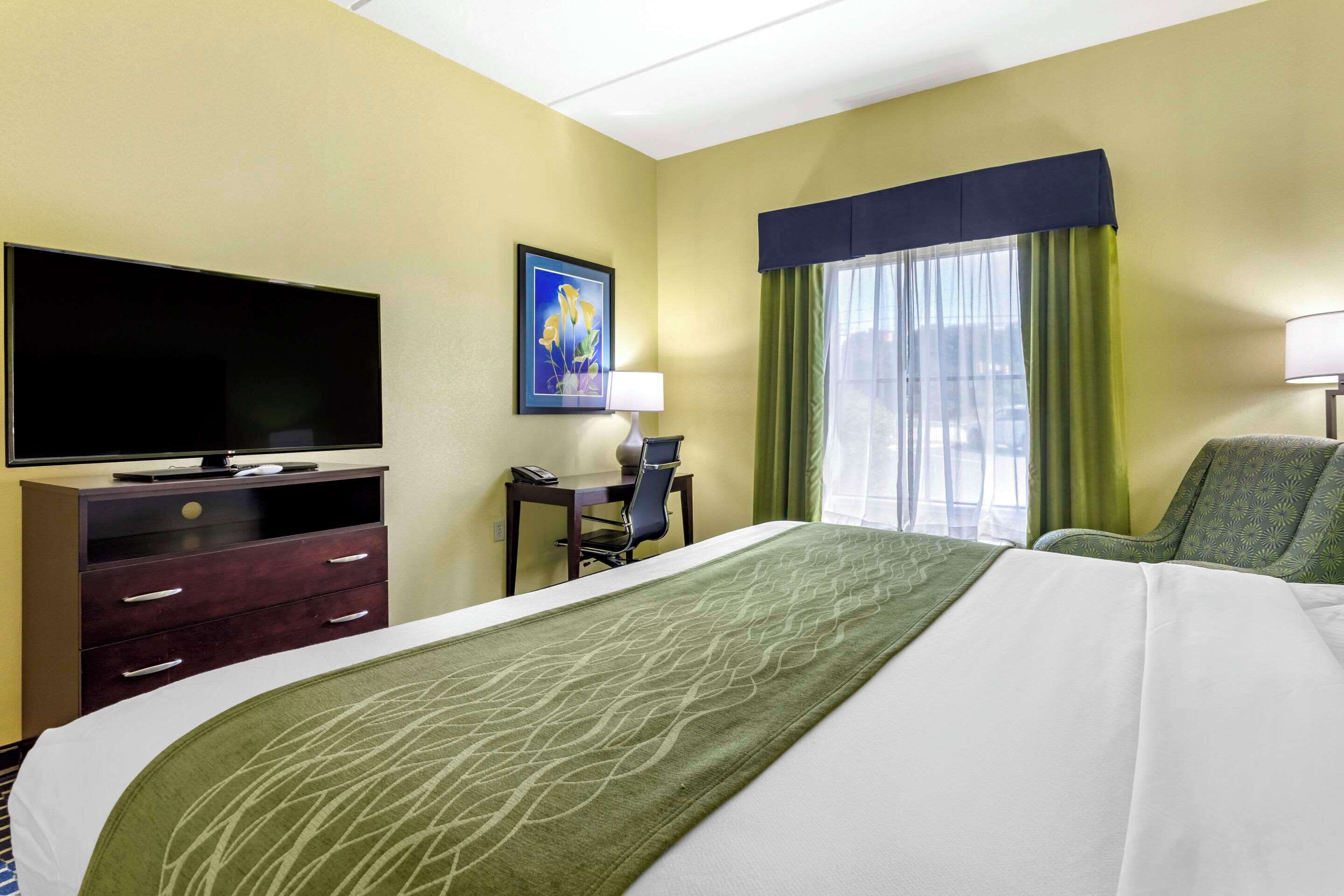 A hotel room with a bed, a TV, a desk with a chair, and a window with curtains.