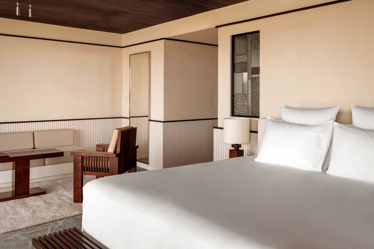 A hotel room with a large bed, a desk, a chair, and a bedside table with a lamp.