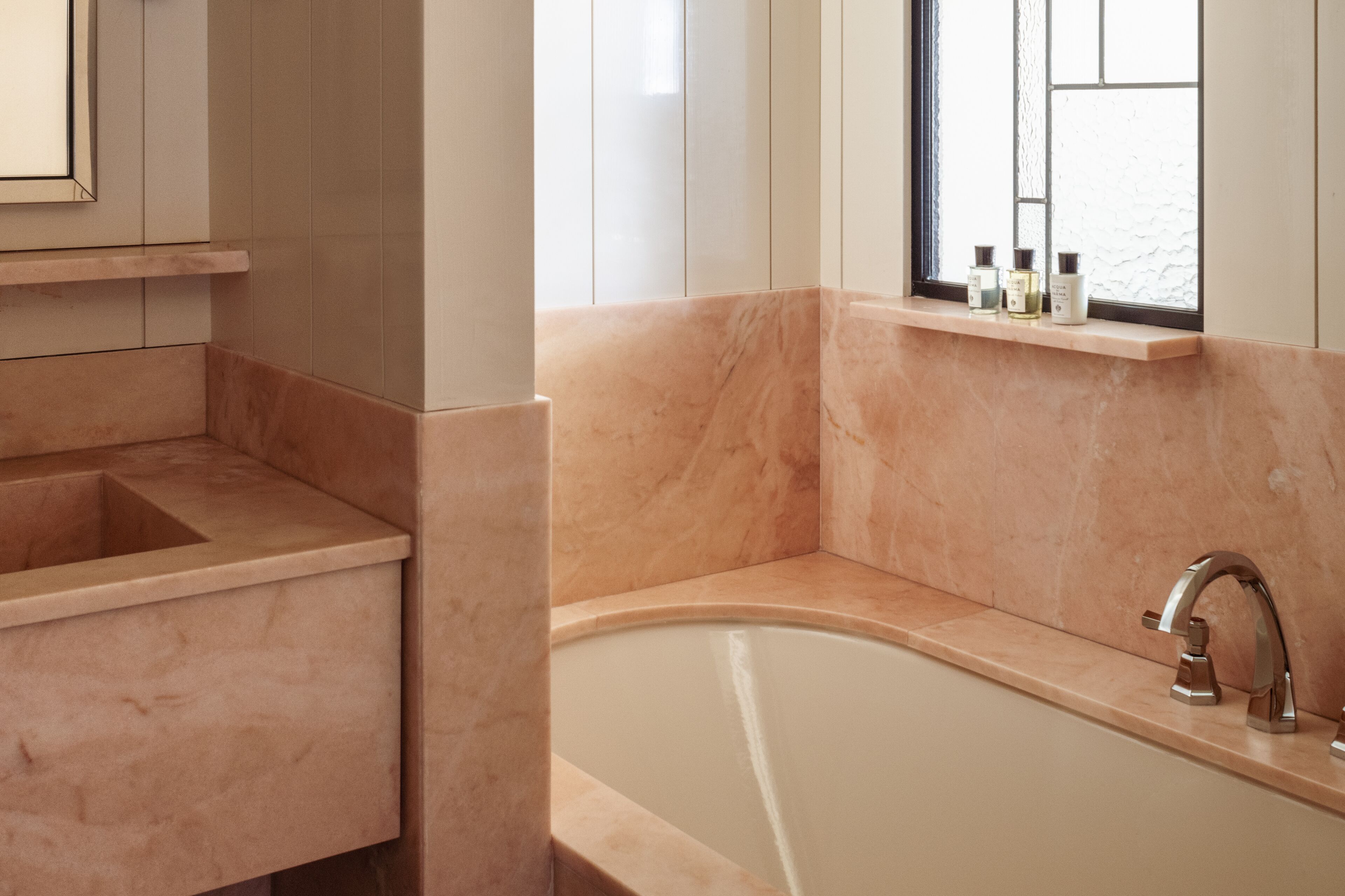 Un baño con una bañera independiente, un tocador con lavabo y una ventana con botellas en el alféizar.