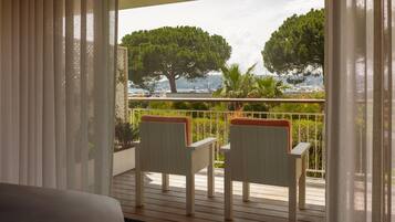 A balcony with two wooden chairs and a view of the sea and trees.