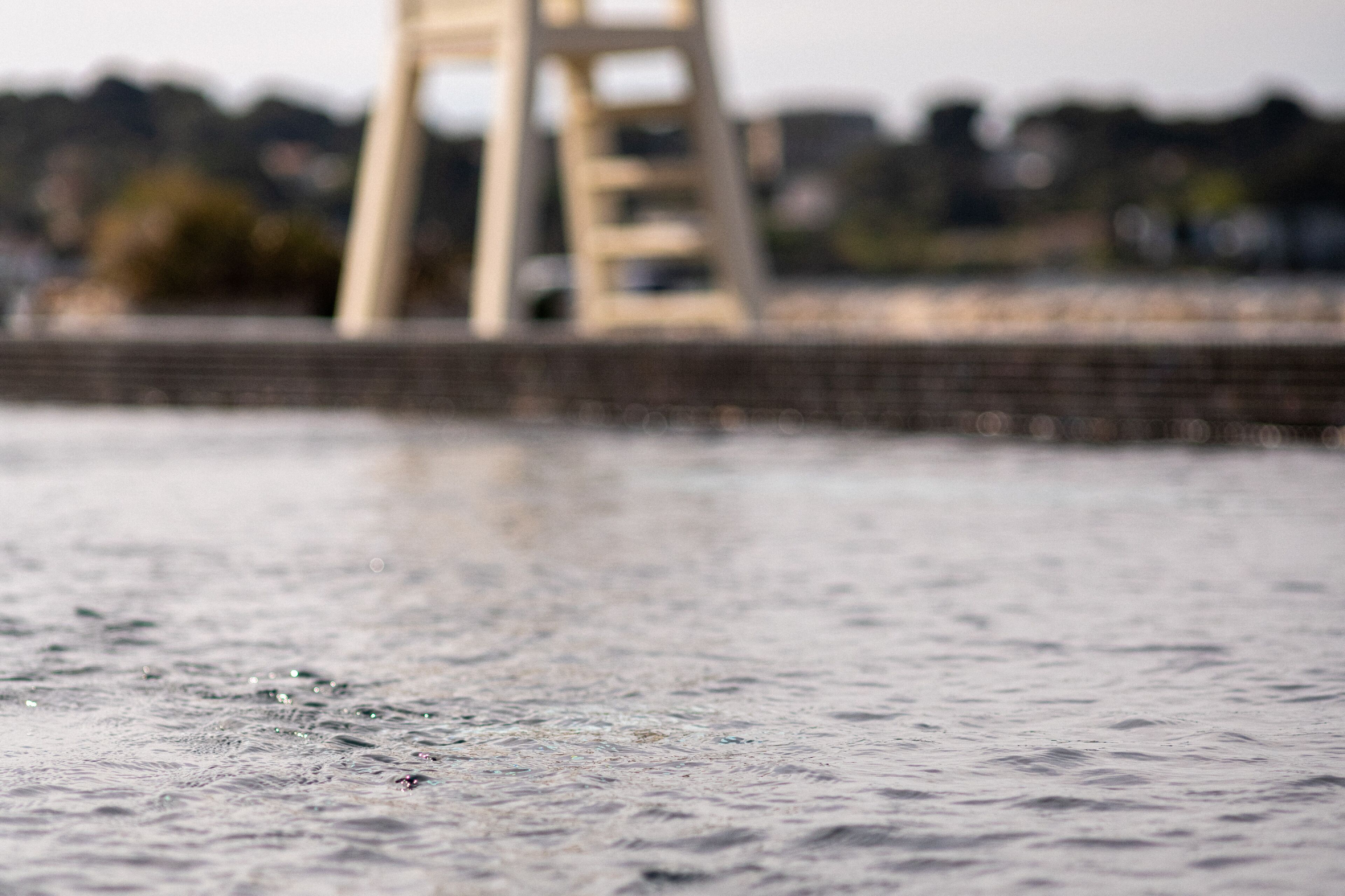 A close-up of a water surface with ripples, a blurred background featuring a bridge structure.