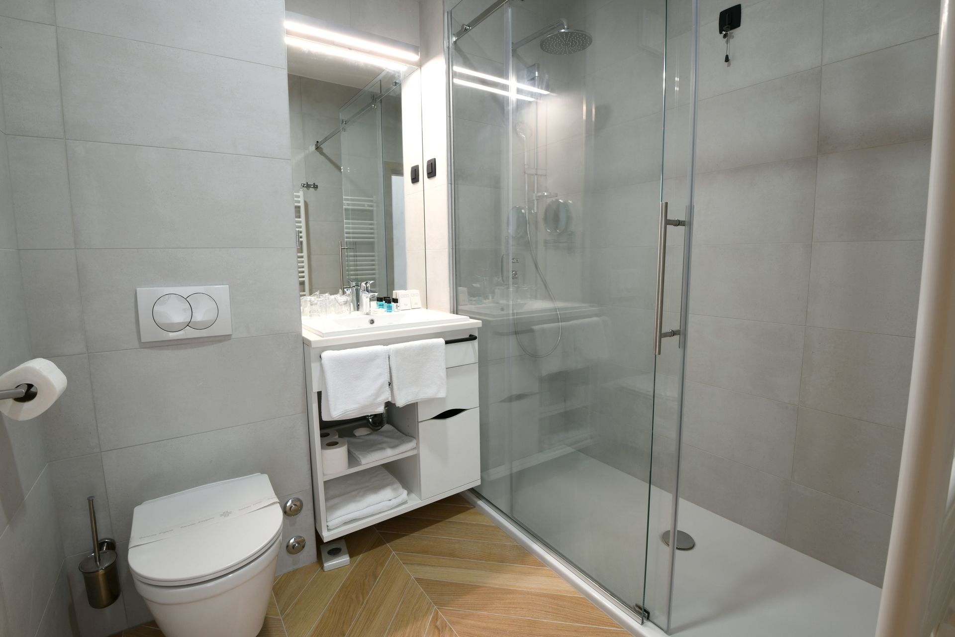 A modern bathroom with a glass-enclosed shower, a white sink with a mirror, and a toilet.