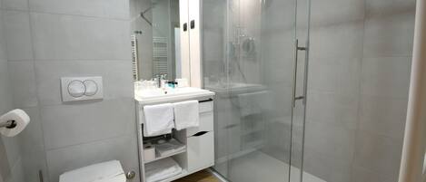 Moderni kylpyhuone, jossa on lasiseinällä varustettu suihku, valkoinen pesuallas peilillä sekä wc-istuin.
