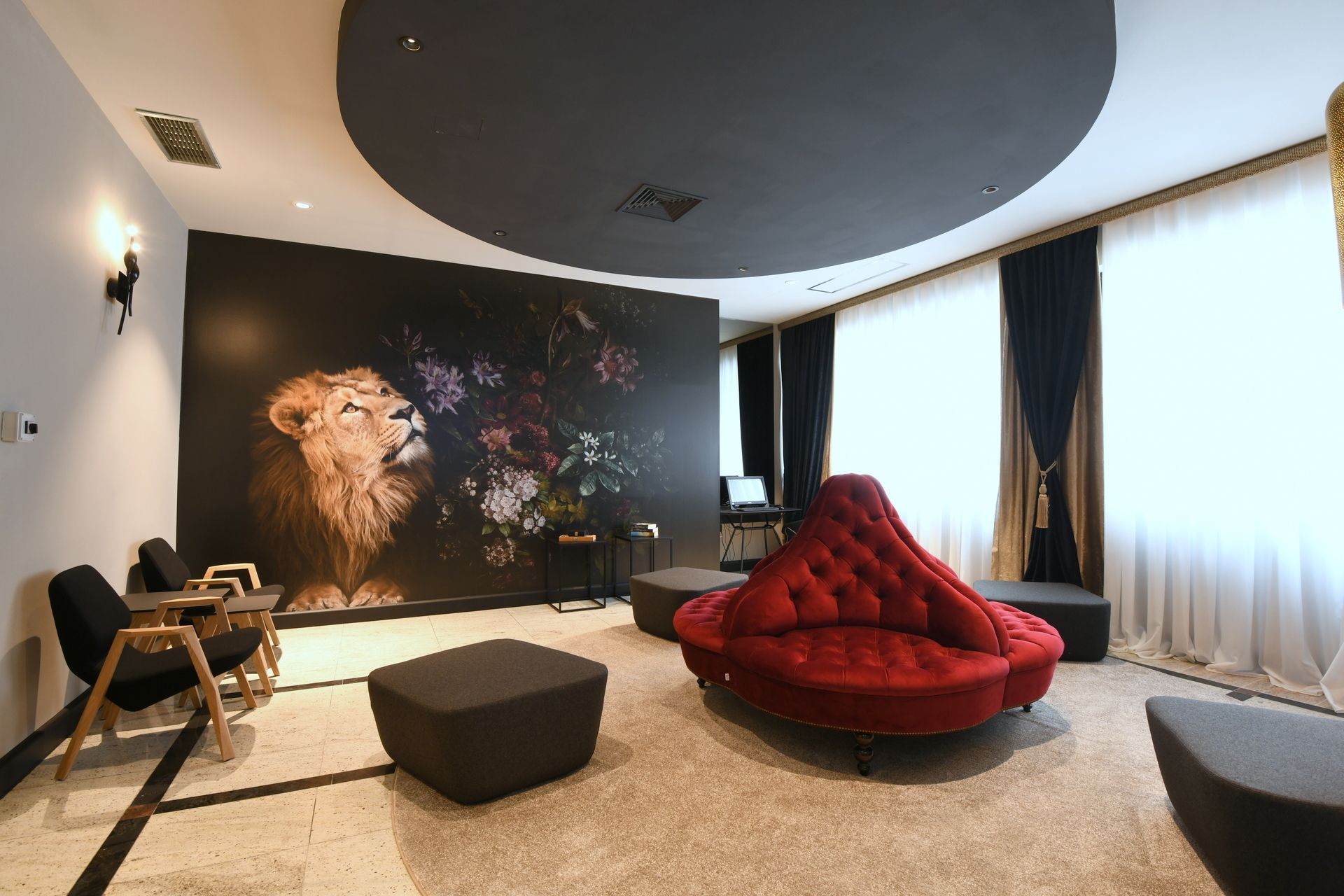 Una sala de estar moderna con un gran mural en la pared, un sofá rojo con capitoné y un rincón de asiento con sillas y otomanas negras.