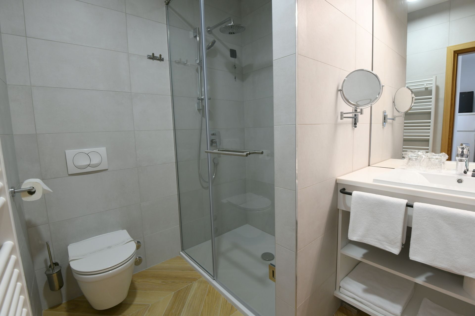 A bathroom with a glass-enclosed shower, a toilet, a sink with a mirror, and a towel rack.