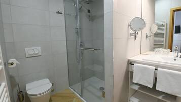 A bathroom with a glass-enclosed shower, a toilet, a sink with a mirror, and a towel rack.