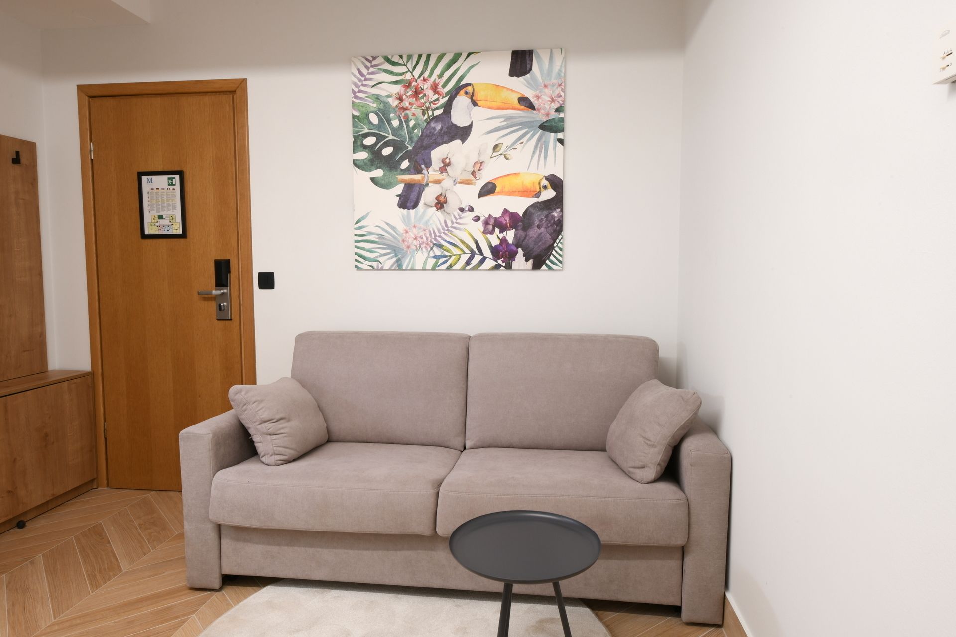 A living room with a beige sofa, a small round table, and a door with a framed map.