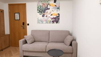 A living room with a beige sofa, a small round table, and a door with a framed map.