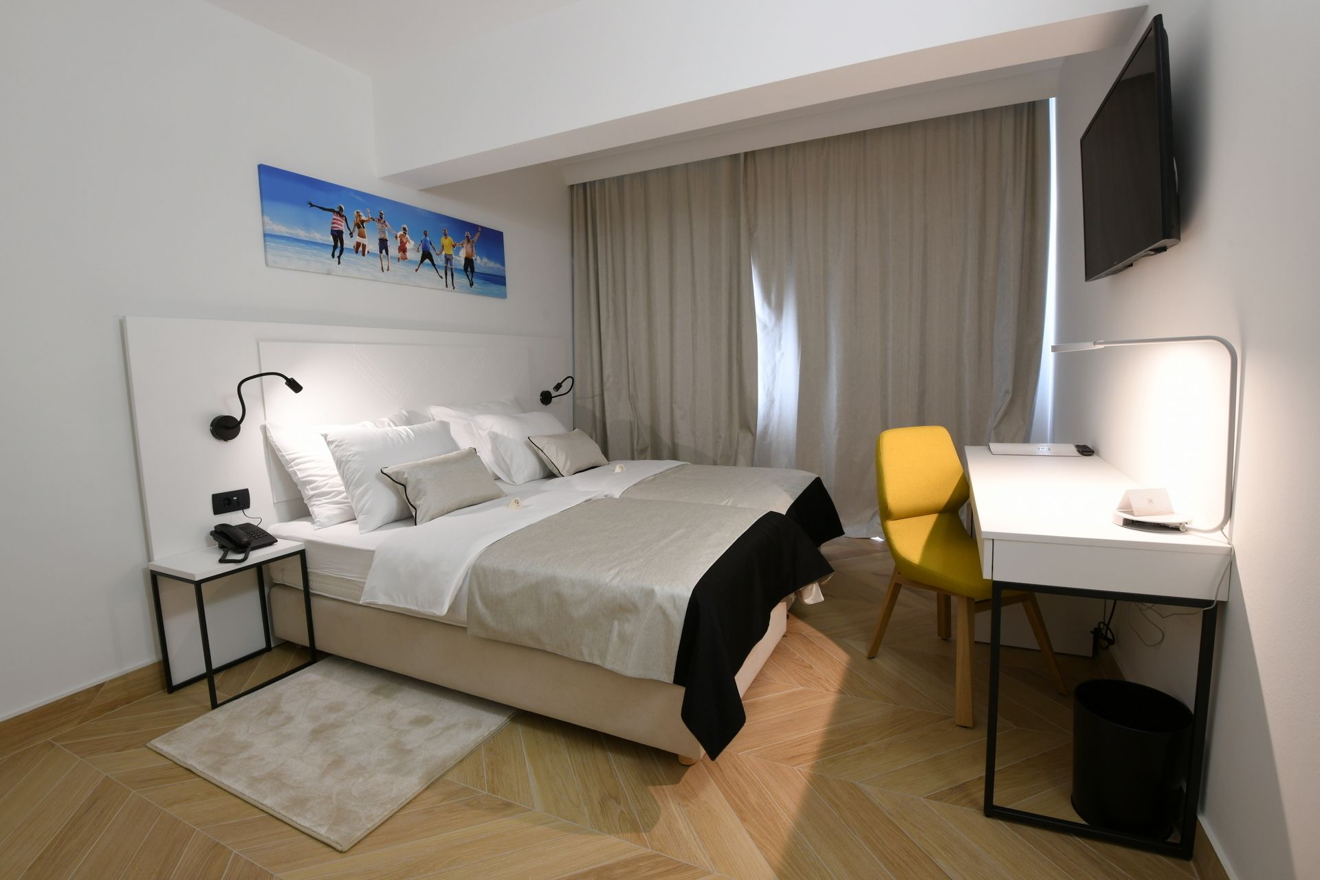 A modern bedroom with a bed, bedside tables, a desk, a chair, a TV, and a painting on the wall.