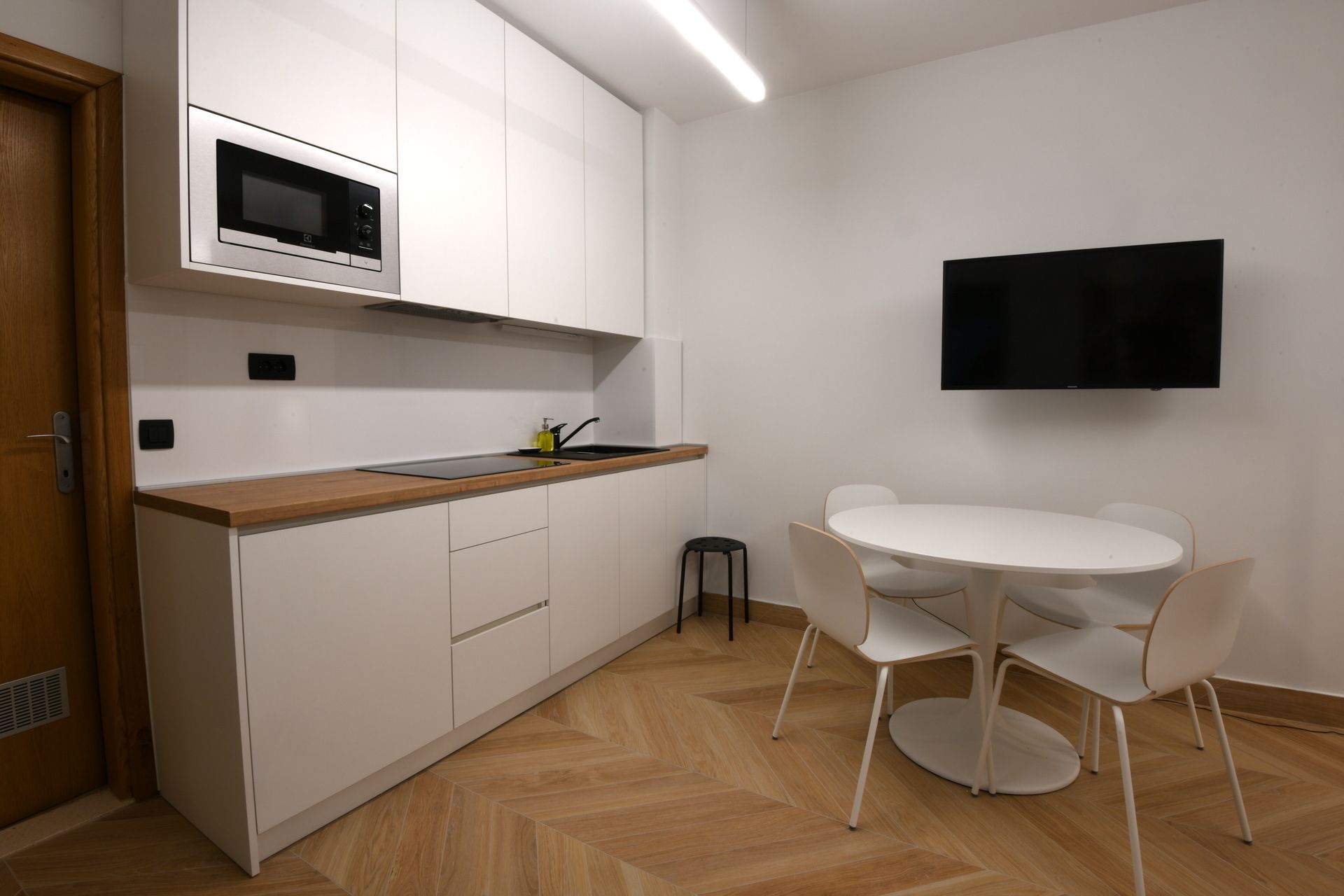 Cocina moderna con armarios blancos, microondas, pileta y zona de comedor con una mesa redonda y sillas.