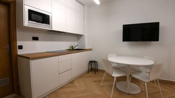 Cocina moderna con armarios blancos, microondas, pileta y zona de comedor con una mesa redonda y sillas.