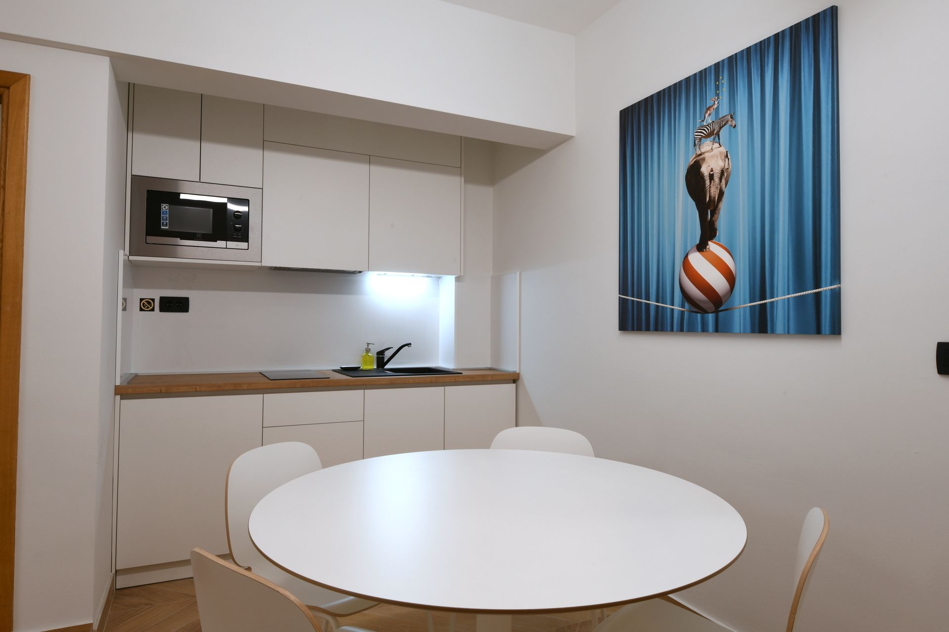 Una cocina moderna con armarios blancos, un microondas y un lavabo. En primer plano, hay una mesa redonda con sillas.