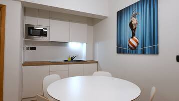 Una cocina moderna con armarios blancos, un microondas y un lavabo. En primer plano, hay una mesa redonda con sillas.