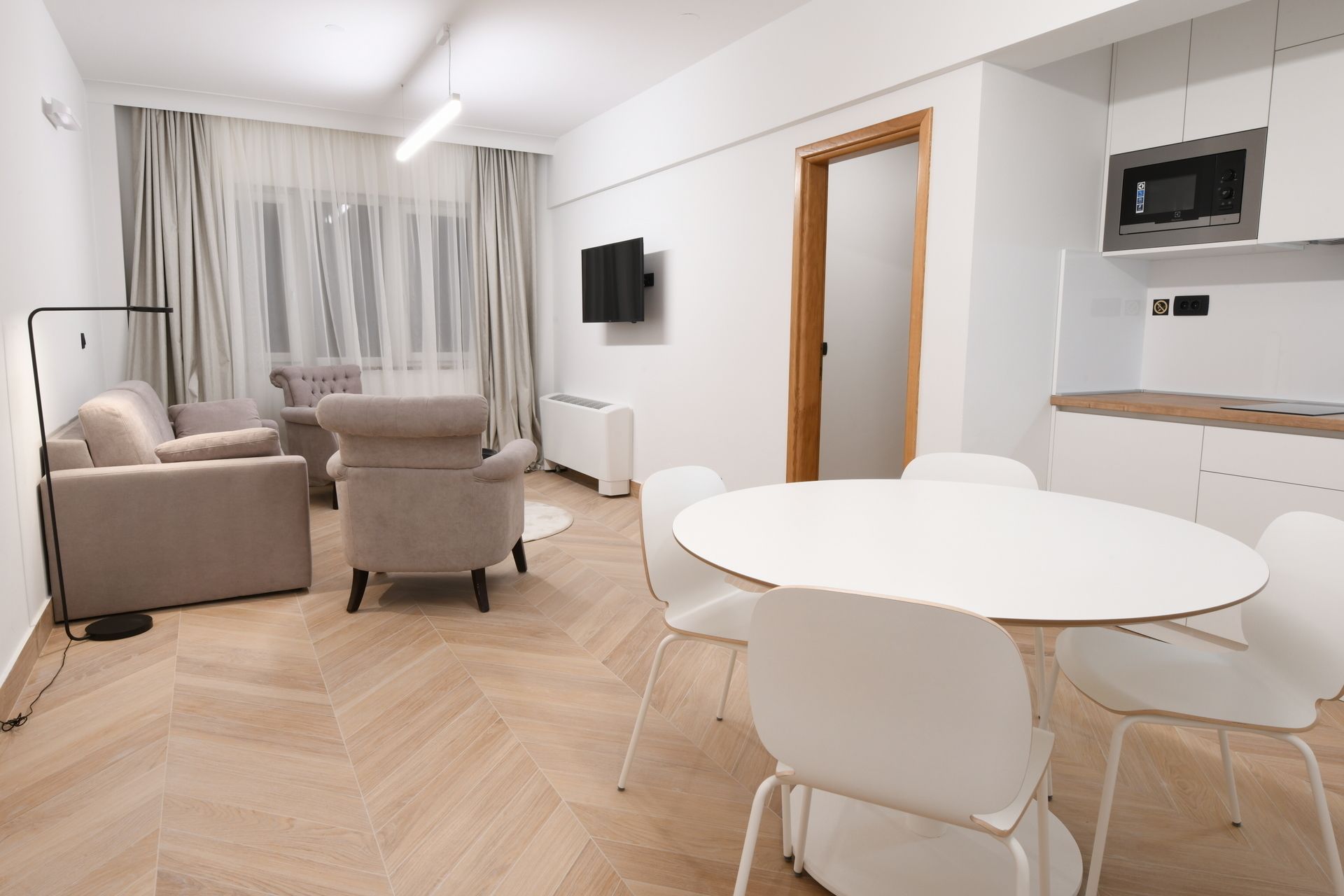 Un salon moderne comprenant un canapé, des fauteuils, une table à manger et un coin cuisine équipé d’un four à micro-ondes.