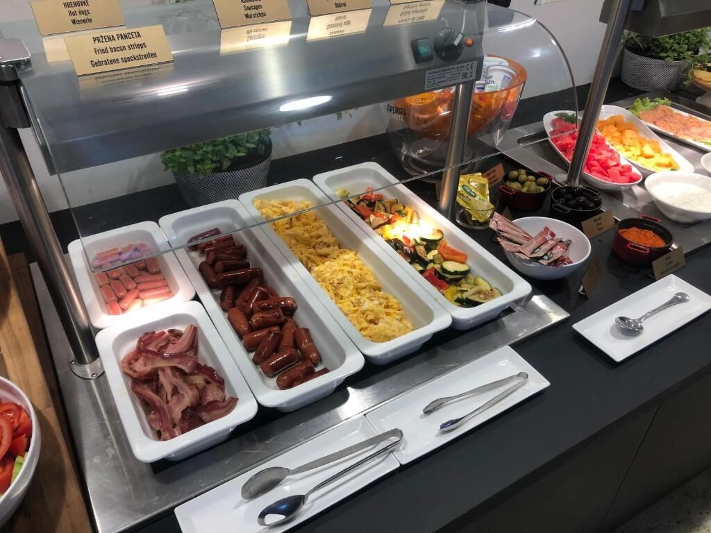 A buffet with various food options including sausages, scrambled eggs, and vegetables.