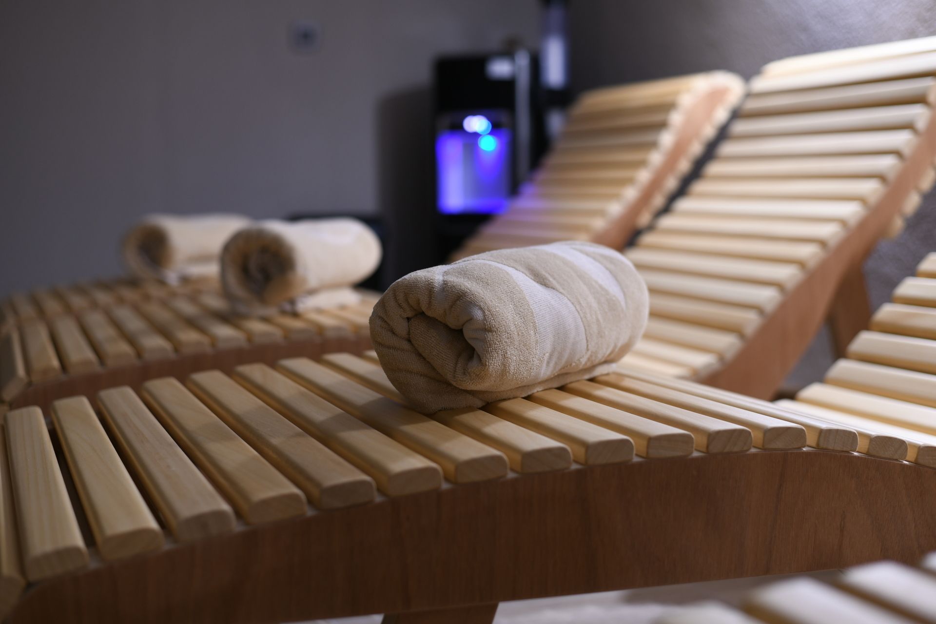 Una fila de sillones de madera con toallas, un panel de control y un dispositivo iluminado en azul al fondo.