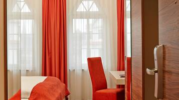 A hotel room with a bed, a chair, a table, and a door.