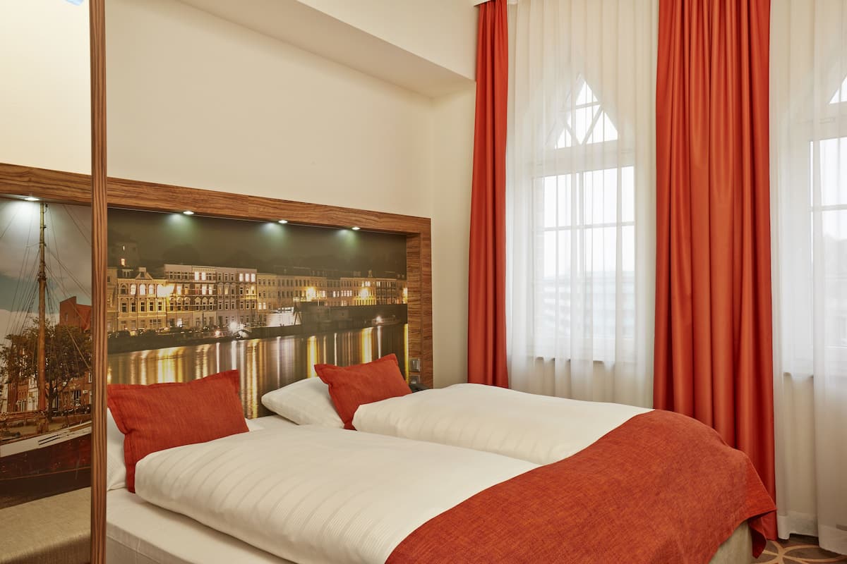 Ein Hotelzimmer mit einem großen Bett, ro weißer Bettwäsche, einem Stadtbild-Wandgemälde und roten Vorhängen.