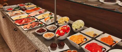 Un buffet proposant une variété de plats, notamment des viandes, des fruits et des pâtisseries.