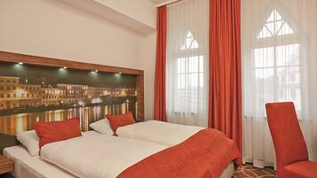 Habitación de hotel con una cama grande, dos almohadas, una silla roja, una mesita de noche y un televisor de pared que muestra un paisaje urbano.