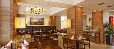 Un comedor de hotel moderno con suelo de madera, varias mesas y lámparas contemporáneas.