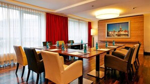 A conference room with a long table, chairs, and a painting on the wall. - H+ Hotel Lübeck (Lübeck)