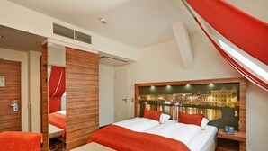 A hotel room with a large bed, a bench, a wooden headboard with a cityscape image, and a red curtain. - H+ Hotel Lübeck (Lübeck)