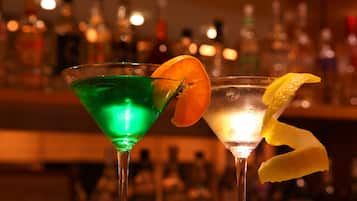 Deux cocktails servis dans des verres à martini, décorés de quelques éléments, sur fond flou de bouteilles de bar.
