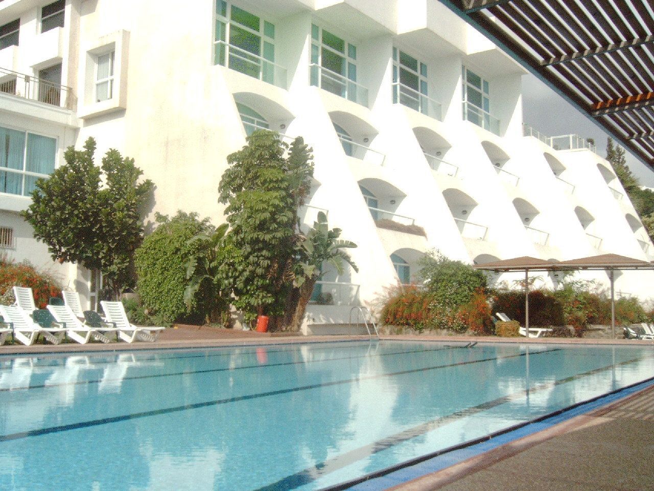 Una piscina con sillones de descanso y un edificio blanco con ventanas arqueadas al fondo.