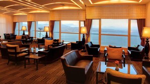 Un vaste espace de détente avec des canapés et des fauteuils en cuir, ainsi que des tables, et de grandes fenêtres offrant une vue sur la mer.