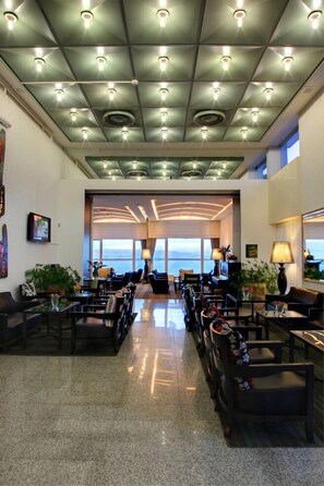 Een ruime lobby met een hoge plafond, meerdere zithoeken en grote ramen met uitzicht op de oceaan.