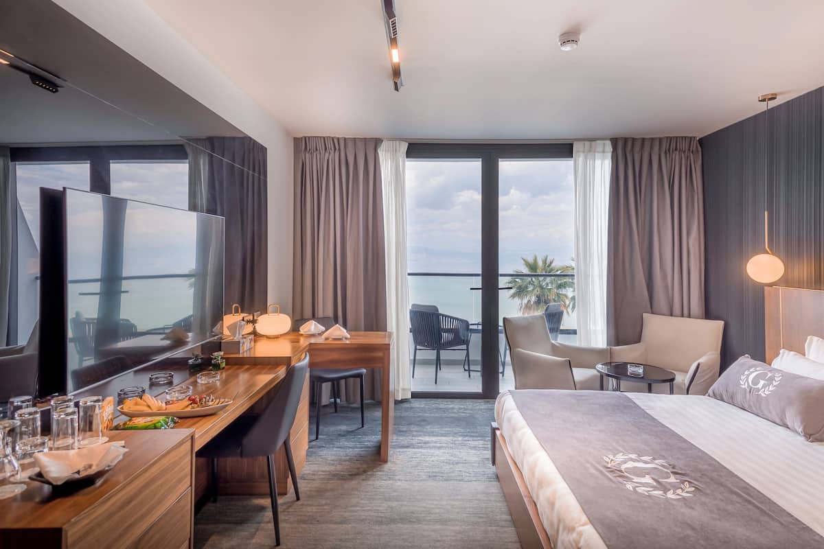 Habitación de hotel con cama, escritorio con silla, televisor y balcón con vistas.