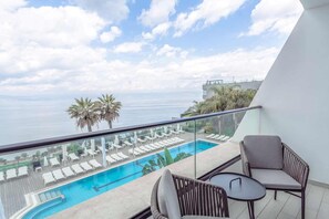 Un balcón con piscina, sillas de descanso y vista al mar.