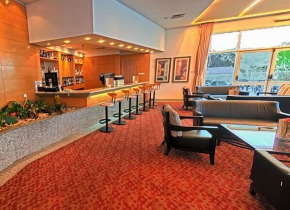 Un vestíbulo de hotel con zona de bar, asientos y alfombra estampada.