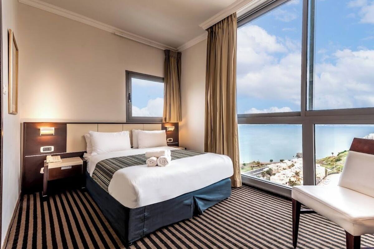 Habitación de hotel con una cama grande, una mesita de noche, una silla y vistas al mar.