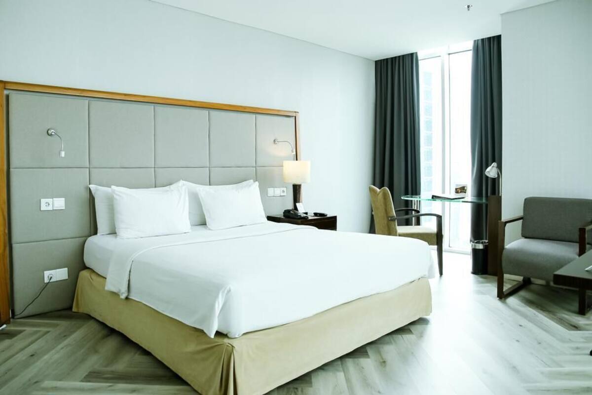 A hotel room with a large bed, a desk, a chair, and a window with curtains.