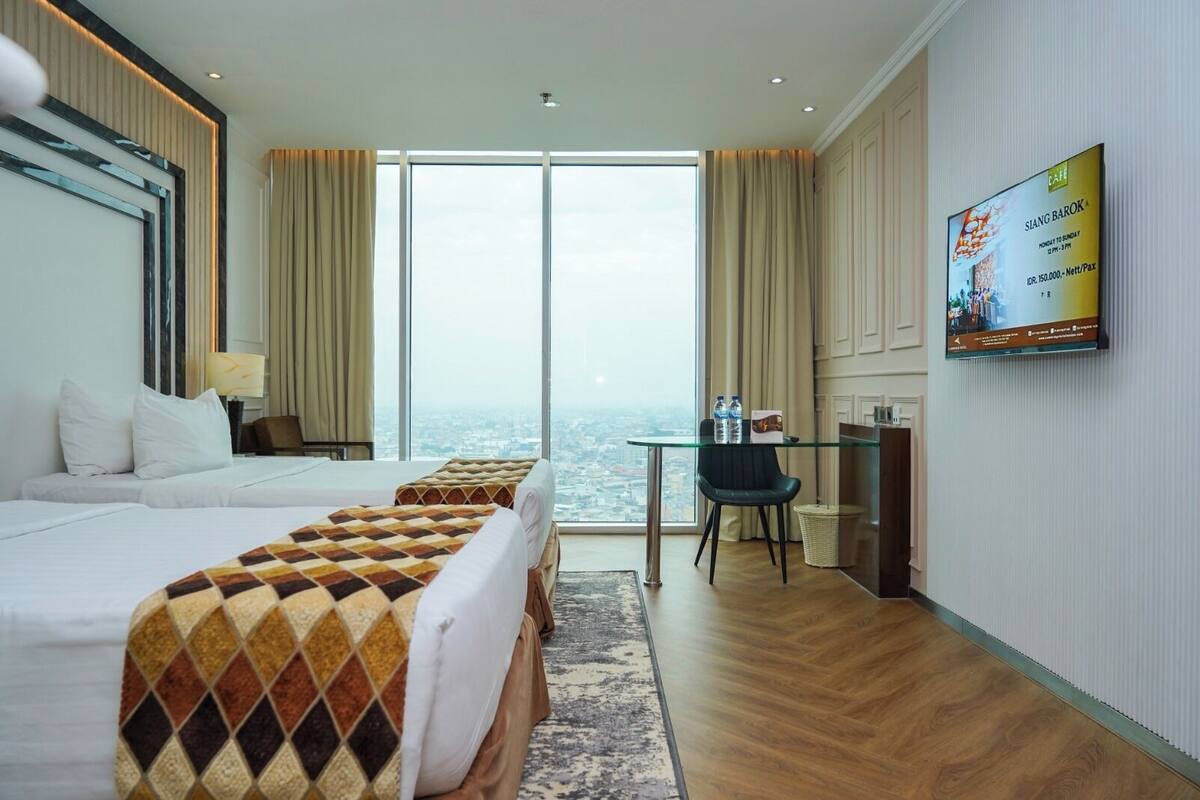 A hotel room with a large bed, a desk, a chair, and a TV on the wall.