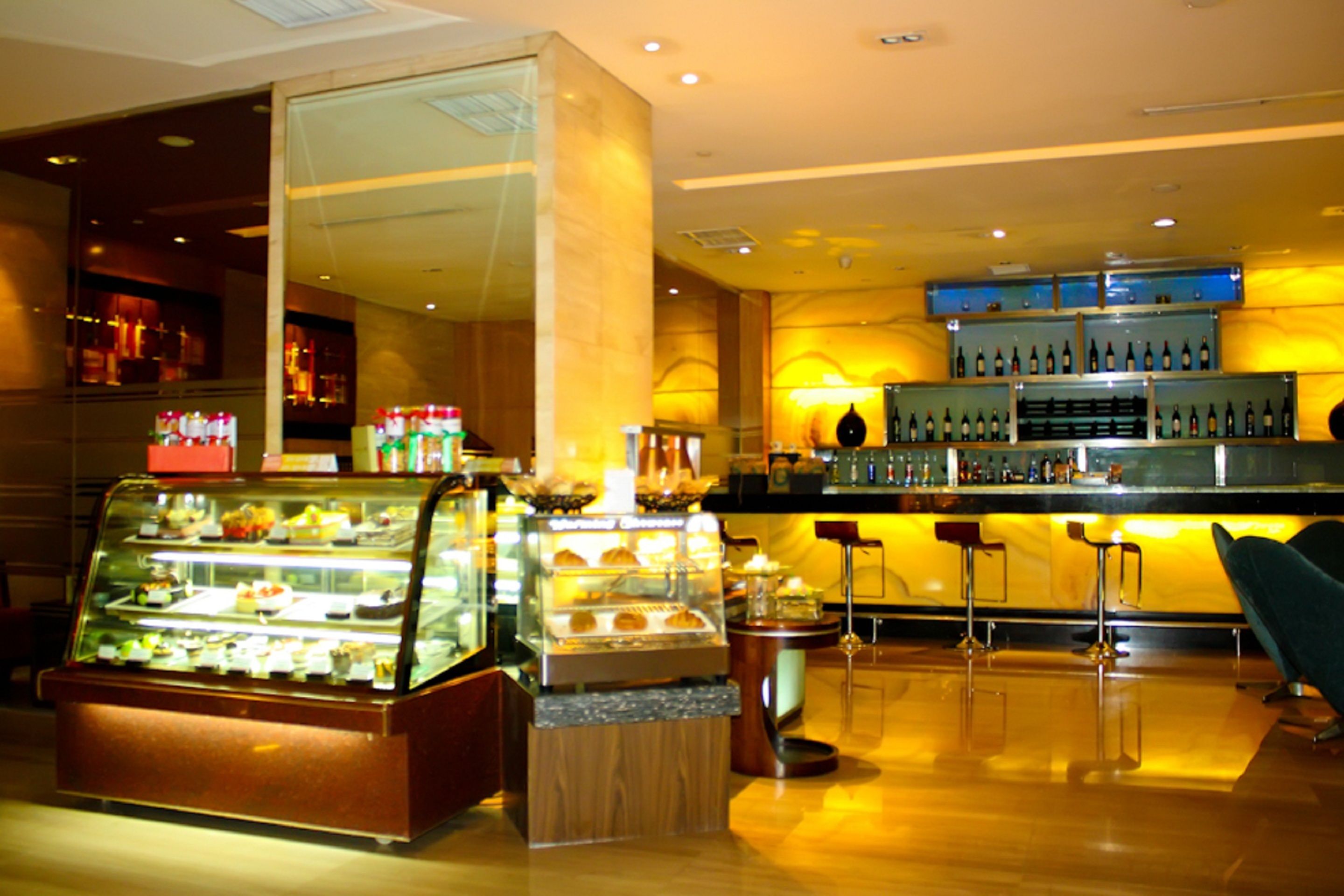 Eine Hotelbar mit einer Vitrine voller Gebäck, einer Bar mit Flaschen und einer Sitzgelegenheit mit Hockern.
