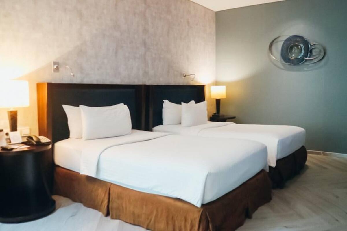 A hotel room with two beds, a headboard, bedside tables, and a wall-mounted light fixture.