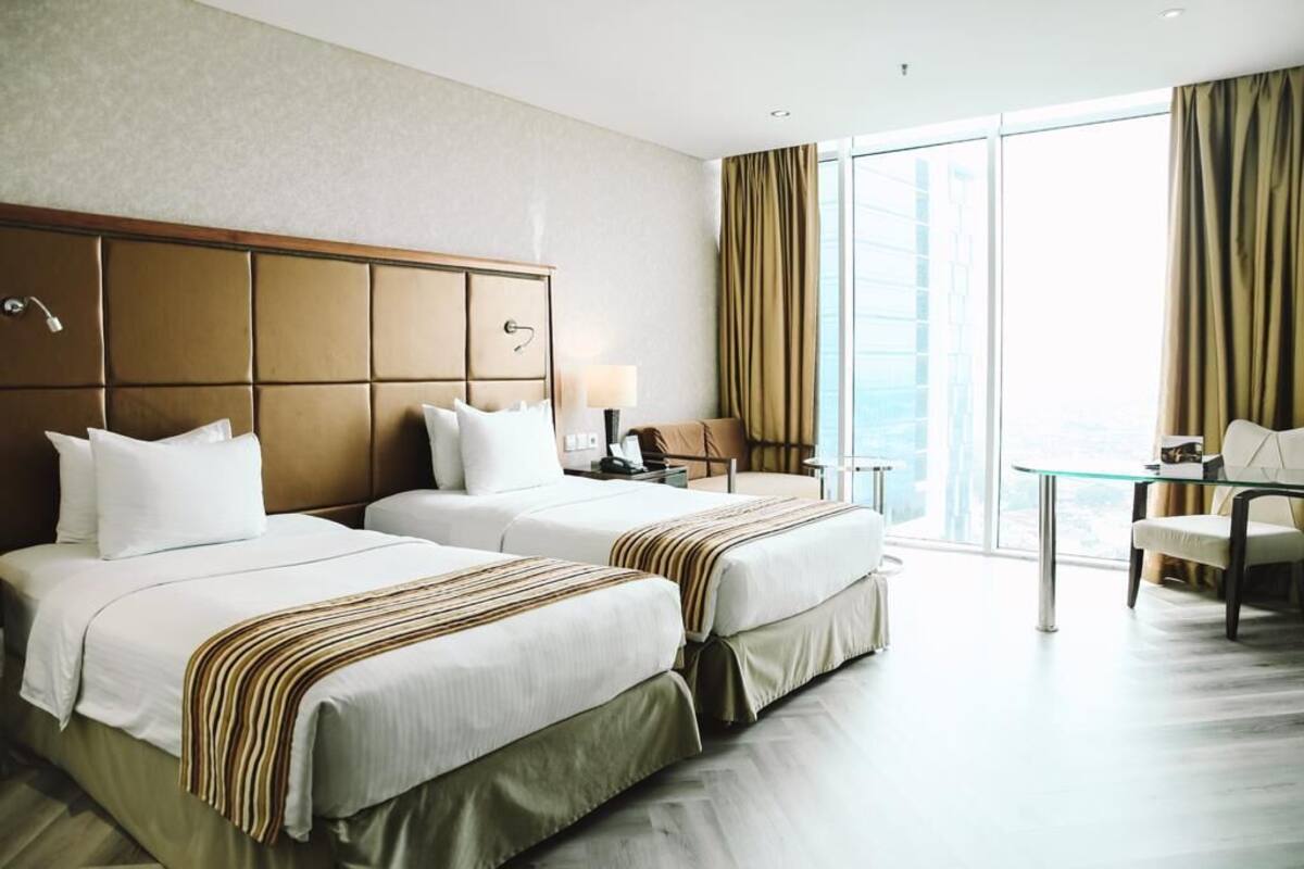 A hotel room with two beds, a glass table, a chair, and a view of the city.