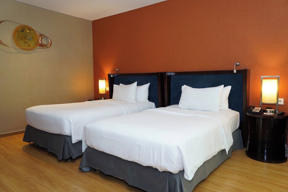 A hotel room with two beds, each with a headboard, bedside tables, and lamps.