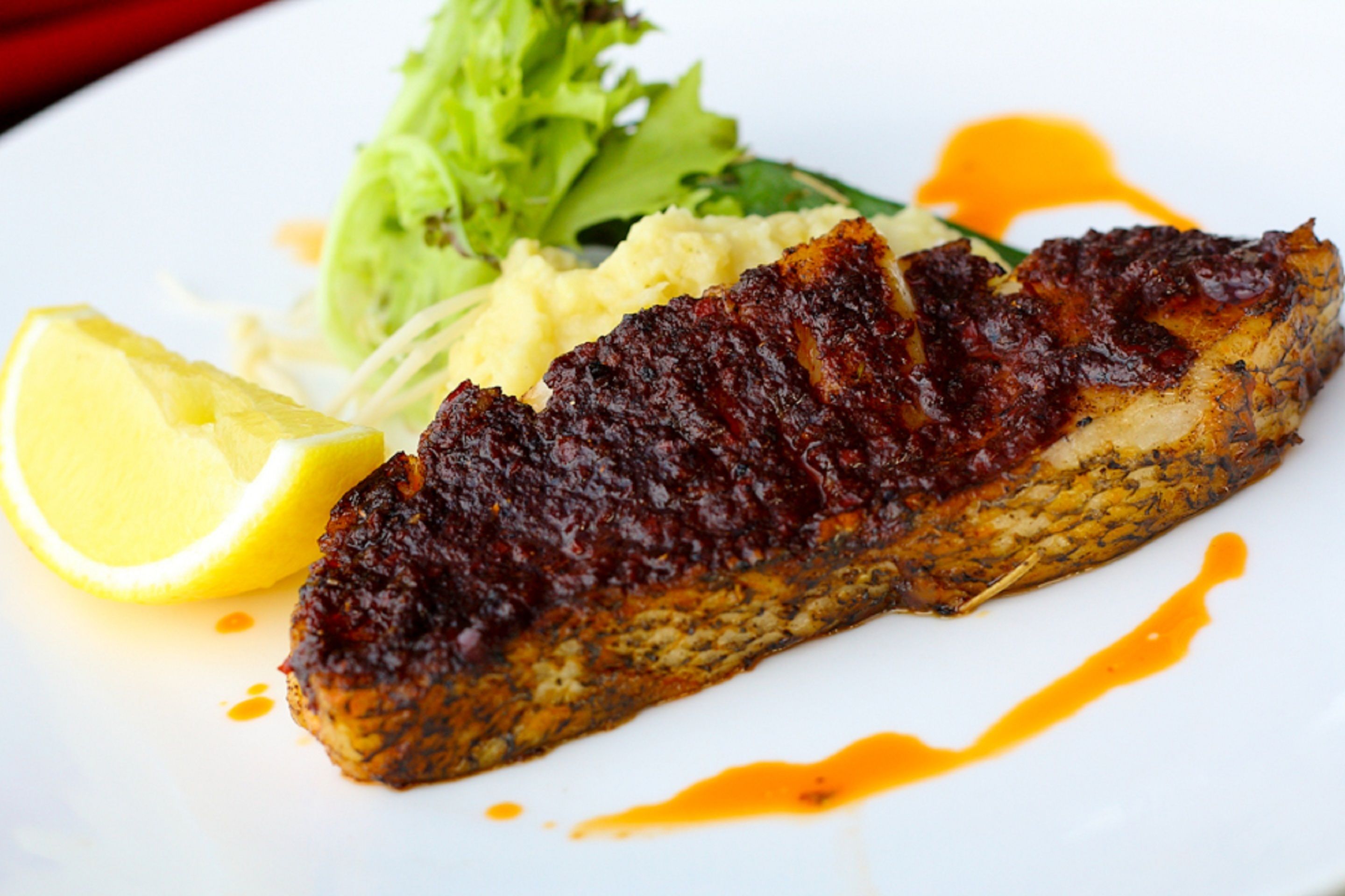 A plate with a glazed fish fillet, a side of mashed potatoes, a lemon wedge, and a green salad.