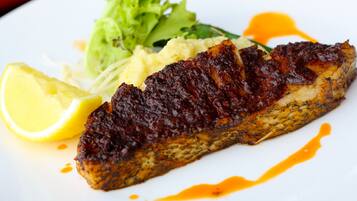 A plate with a glazed fish fillet, a side of mashed potatoes, a lemon wedge, and a green salad.