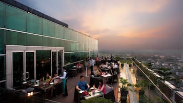 An outdoor dining area with tables and chairs, surrounded by glass walls and potted plants.